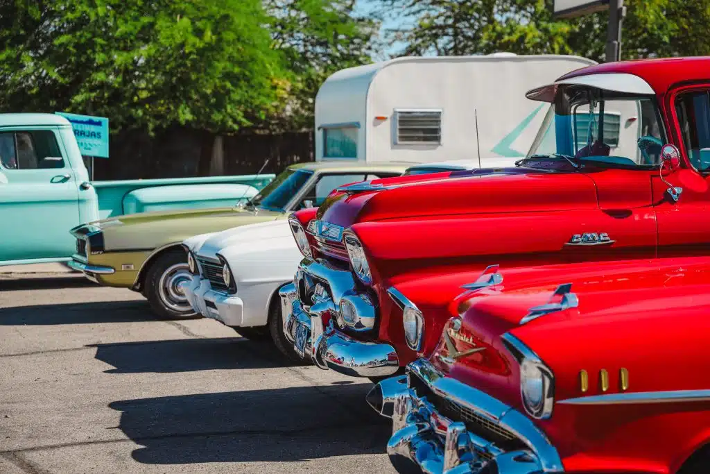 A vibrant lineup of vintage classic cars, including bright red Chevrolet and GMC trucks, parked at the Luna y Sol Community Habitat event under the Arizona sun