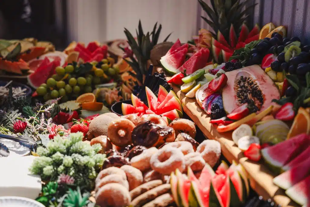 A vibrant spread of fresh fruit and pastries at the Luna y Sol Community Habitat event, featuring watermelon, papaya, kiwi, grapes, and donuts arranged in a colorful, abundant display