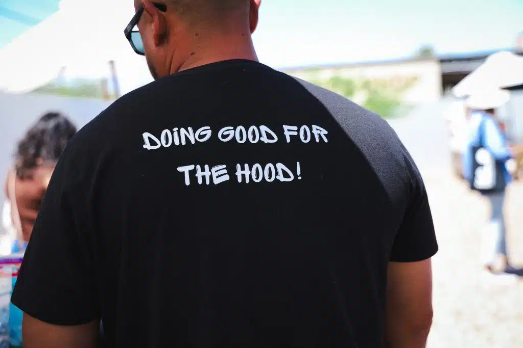Close up of a man wearing a black T shirt that reads “DOING GOOD FOR THE HOOD!” at the Luna y Sol Community Habitat event