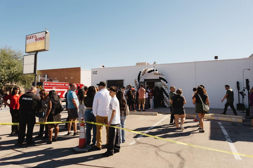 Neighbors line up in the parking lot before the balloon arch at 137, with a Luna y Sol Cafe sign and a fire truck at left.